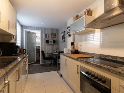 Cuisine équipée avec meubles crème, plans de travail en granit et appareils inox intégrés. Un coin repas avec table en verre et papier peint rayé se trouve à l'arrière-plan.
