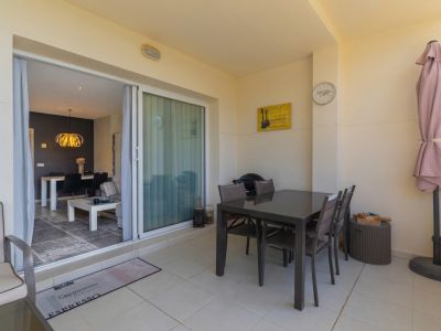 Terrasse extérieure avec carrelage clair, une table à manger sombre et un parasol replié, reliée à un salon intérieur avec luminaire suspendu doré.