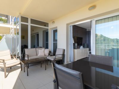 Vaste terrasse extérieure aménagée avec un coin salon et un espace repas distincts. Elle dispose d'un carrelage clair et d'un accès direct à l'intérieur par des baies vitrées.