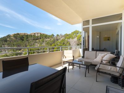 Vaste terrasse extérieure avec mobilier de salle à manger et de salon, offrant des vues sur une colline verdoyante de pins et des bâtiments lointains.