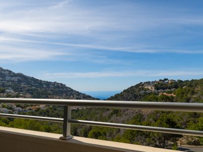 Vue panoramique depuis la terrasse avec balustrade métallique, présentant des collines verdoyantes parsemées de maisons et la mer Méditerranée au loin.