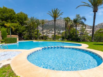 Complexe de piscines à plusieurs niveaux avec bassin pour enfants, entouré de palmiers et pelouse. Vues panoramiques sur les montagnes sous un ciel bleu clair.