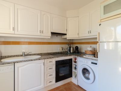 Cuisine fonctionnelle avec placards blancs à panneaux, plan de travail effet granit, électroménager intégré et carrelage mural avec bande décorative orange.