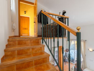 Escalier intérieur avec marches carrelées en terre cuite et bordures en bois, doté d'une balustrade en métal vert foncé et d'une main courante en bois. Il mène à une entrée avec mur jaune et porte en bois.