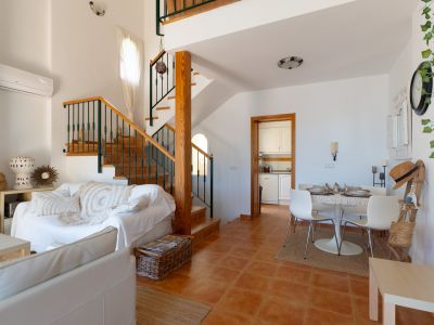 Espace salon-salle à manger ouvert avec carrelage en terre cuite et escalier en bois à balustrade métallique. Comprend un coin repas et un salon lumineux.