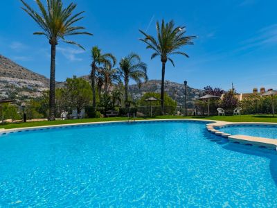 Piscine à plusieurs niveaux avec carrelage mosaïque bleu vif, entourée d'une pelouse verdoyante et de palmiers, avec les montagnes d'Altea Hills en arrière-plan.