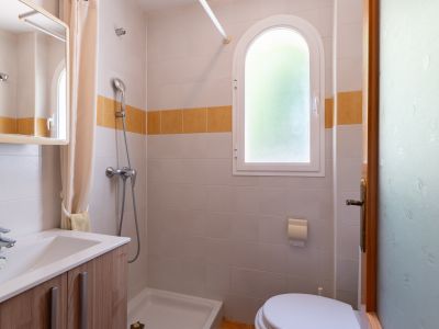 Salle de bain compacte avec fenêtre arquée en verre dépoli, murs carrelés bicolores avec bande orange, douche avec receveur et meuble-lavabo en bois.