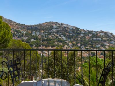 Terrasse avec balustrade en fer forgé et mobilier de jardin, offrant une vue dégagée sur l'urbanisation résidentielle à flanc de colline.