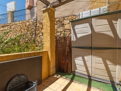 Terrasse extérieure carrelée avec un meuble de rangement pratique, un mur en pierre naturelle orné de plantes fleuries et une pergola en bois.