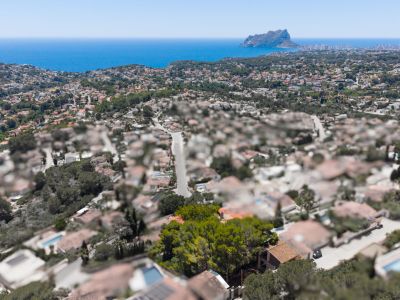 Vue aérienne d'un quartier résidentiel côtier avec la mer Méditerranée et le Peñón de Ifach au loin, sous un ciel bleu clair.