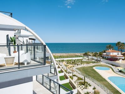Balcon moderne avec garde-corps en verre et mobilier extérieur blanc, offrant des vues panoramiques sur la mer Méditerranée, les piscines et les jardins paysagers.