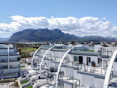 Bâtiment d'appartements contemporain avec façades blanches incurvées, terrasses vitrées avec gazon artificiel et vues étendues sur la chaîne de montagnes.