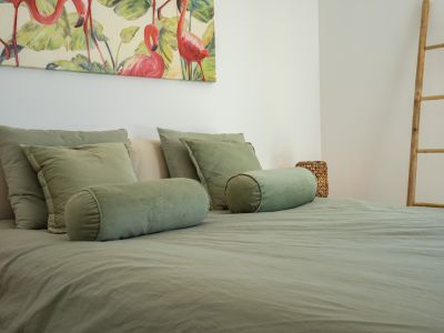 Chambre à coucher avec un lit habillé de linge vert sauge, rehaussée par une grande toile de flamants roses et une échelle décorative en bambou.