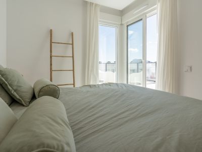 Chambre lumineuse avec lit en parure vert sauge, grandes portes vitrées donnant sur une terrasse et échelle décorative en bois.
