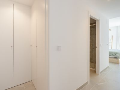 Couloir avec placards intégrés blancs, sol carrelé gris clair, et vues sur une salle de bain avec douche carrelée sombre et une chambre avec vue sur mer.