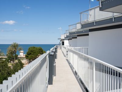 Couloir extérieur carrelé de clair avec balustrades modernes, offrant une vue directe sur la mer Méditerranée et des palmiers.