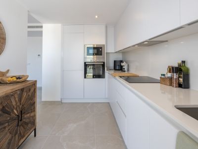 Cuisine moderne avec des armoires blanches sans poignées, des appareils électroménagers intégrés en acier et des plans de travail clairs. Le sol carrelé contraste avec une console en bois rustique.
