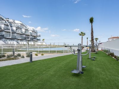 Espace fitness extérieur avec gazon artificiel et équipements, jouxtant la piscine commune et l'immeuble d'appartements moderne, avec vue sur la mer.