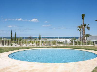 Piscine circulaire avec margelle pavée, entourée de pelouse et d'un jardin méditerranéen avec palmiers, offrant une vue sur la mer.