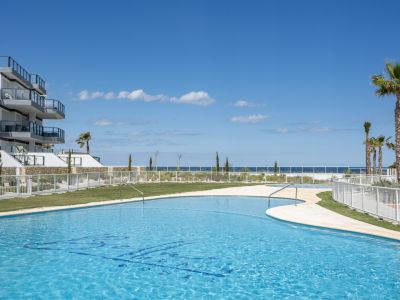 Piscine commune aux formes courbes avec vue sur la mer, entourée de pelouses et de la façade moderne de l'immeuble d'appartements.