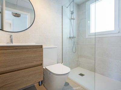 Salle de bain moderne avec meuble-lavabo suspendu en bois clair, toilettes et douche à l'italienne dotée d'une paroi vitrée et d'une fenêtre.