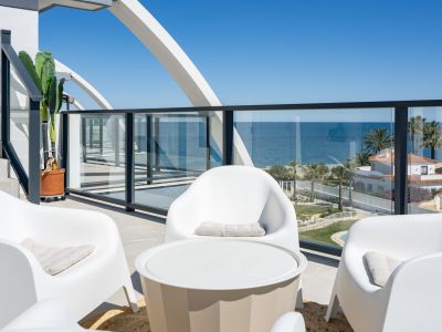 Vaste terrasse avec mobilier blanc contemporain et balustrade en verre, offrant des vues panoramiques sur la mer Méditerranée et la côte, sous un arc structurel distinctif.