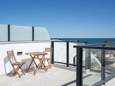 Vaste terrasse carrelée claire, mobilier extérieur en bois et balustrades modernes en verre encadrant une vue panoramique sur la mer Méditerranée.