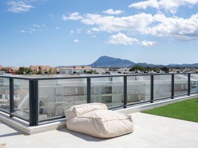 Vaste terrasse sur le toit avec carrelage et gazon artificiel, délimitée par une balustrade en verre, offrant une vue sur la montagne et la ville.
