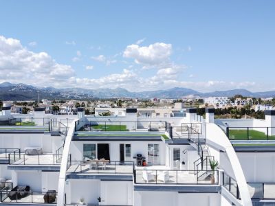 Vue aérienne d'appartements modernes à plusieurs niveaux, avec terrasses spacieuses, balustrades en verre, pelouses artificielles et mobilier extérieur, devant un paysage de montagnes et ville.