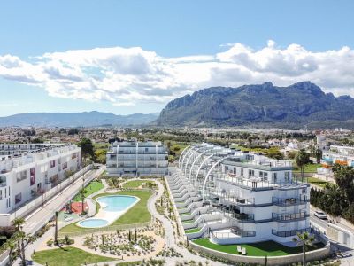 Vue aérienne d'un complexe résidentiel moderne avec deux bâtiments blancs distincts, piscines communes, jardins paysagers et aire de jeux, avec des montagnes en arrière-plan.