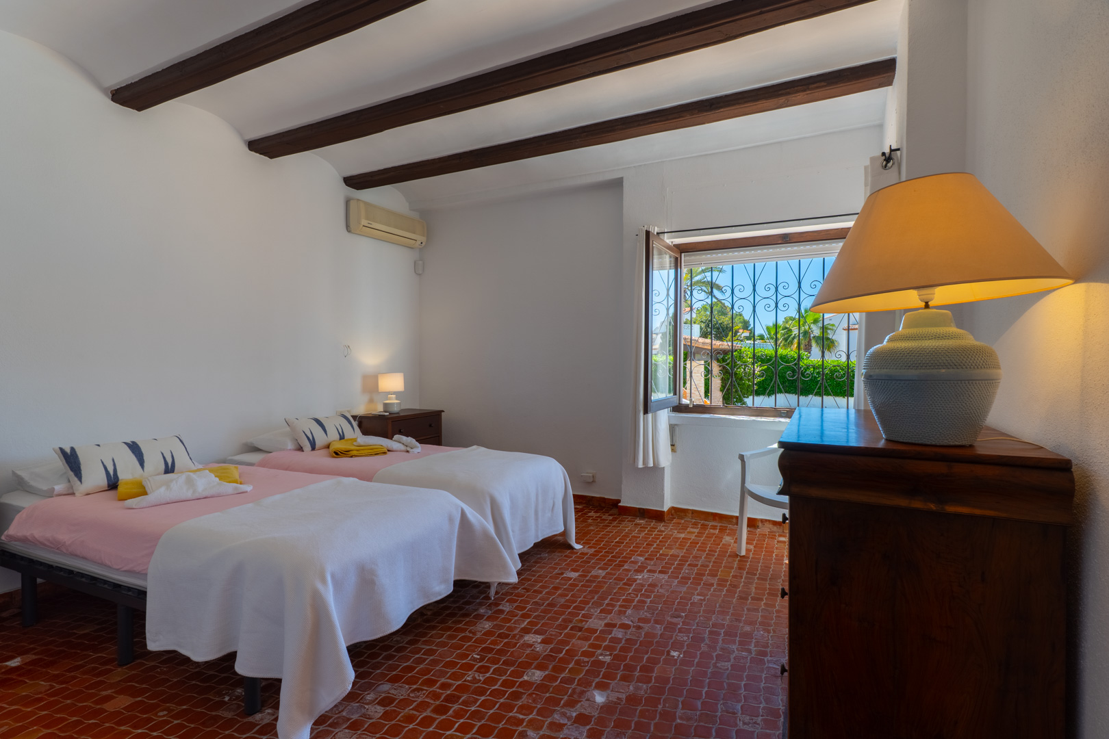 Chambre avec lits jumeaux, poutres apparentes et sol en terre cuite. Vues extérieures.