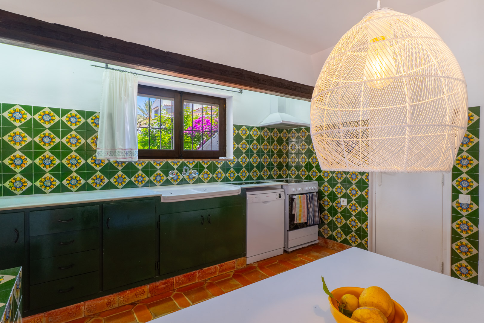 Cuisine avec carreaux décoratifs, meubles vert foncé et suspension en osier.