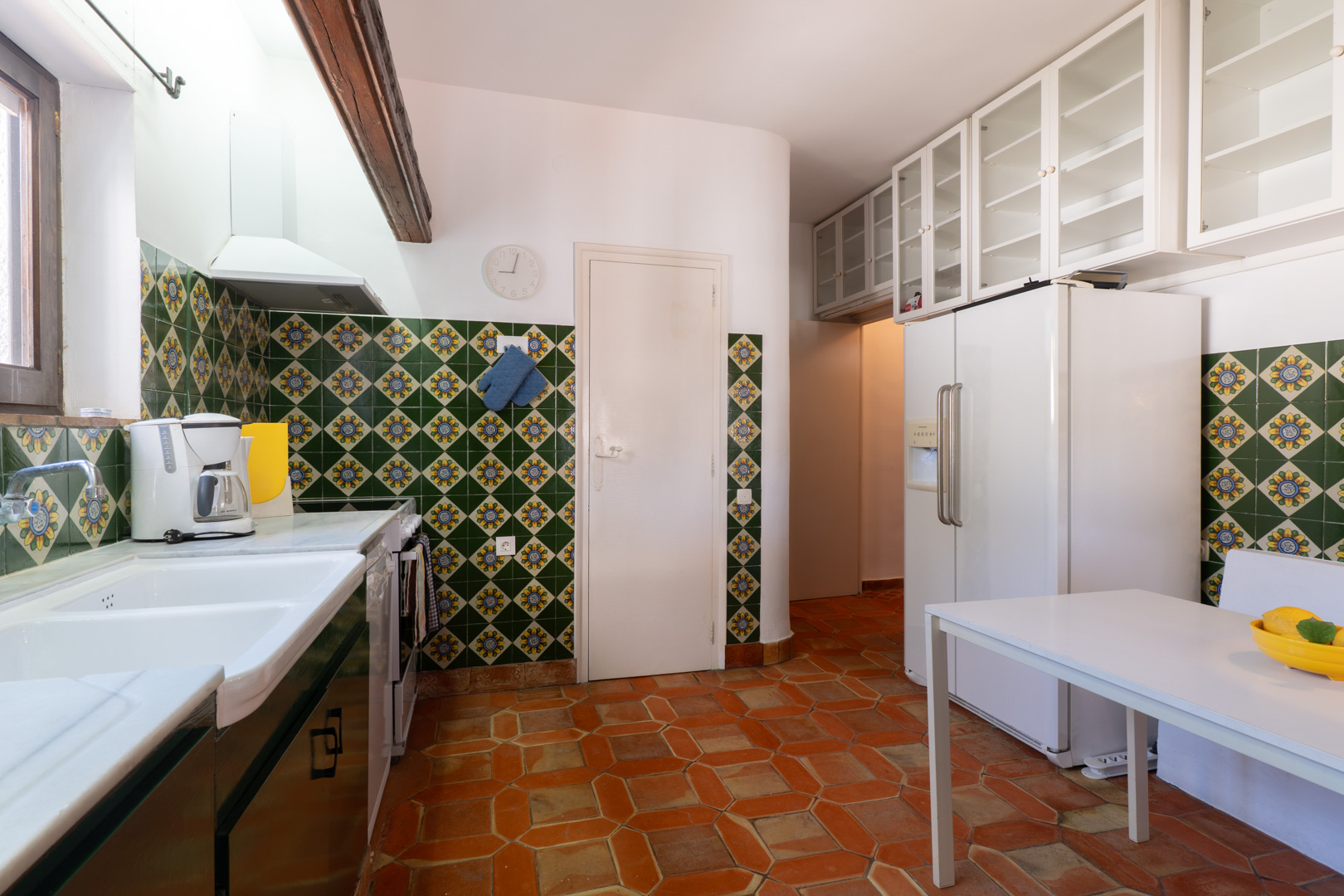 Cuisine avec carrelage décoratif, sol en terre cuite et placards hauts blancs.