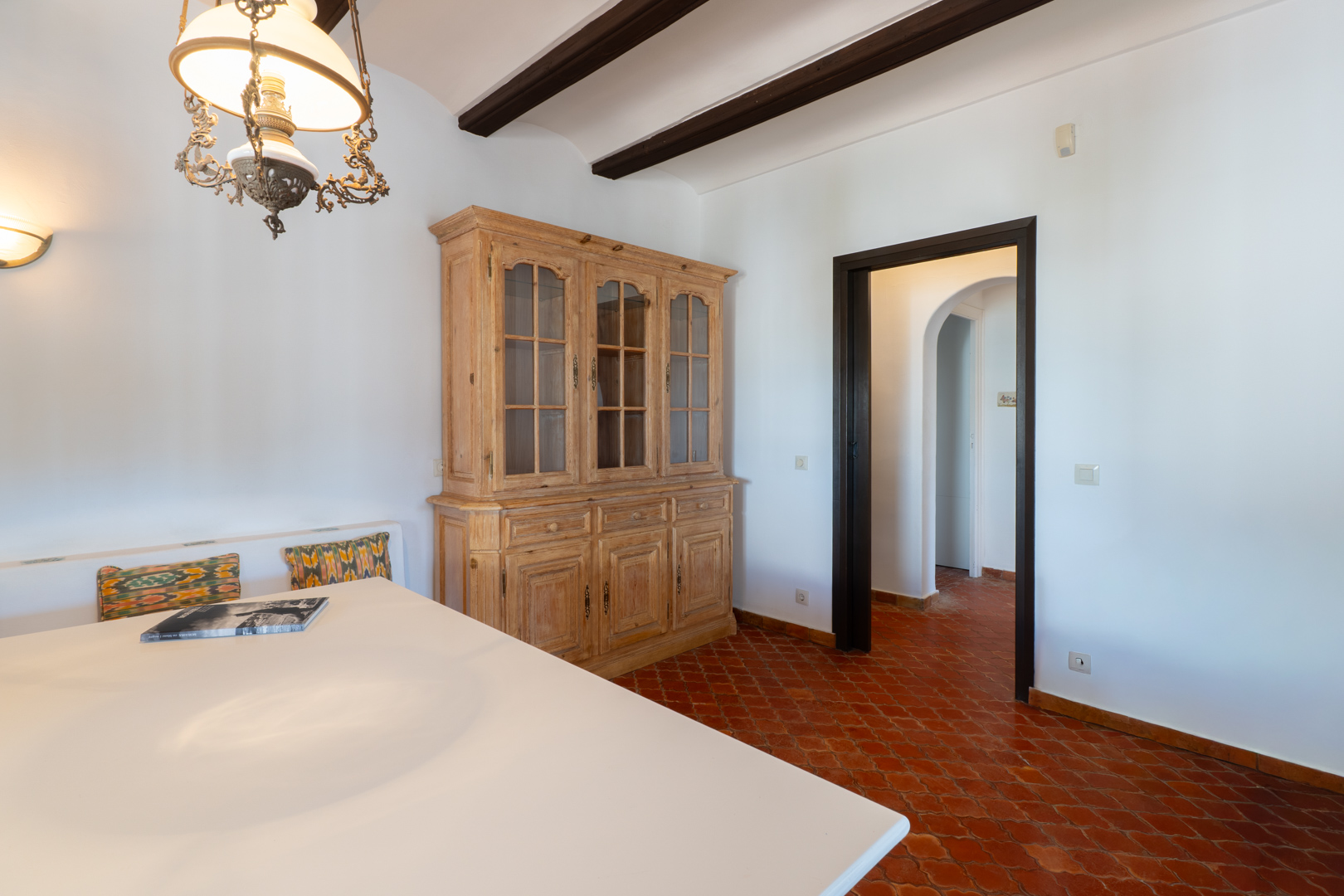 Détail de la salle à manger avec buffet en bois clair et sol en terre cuite.