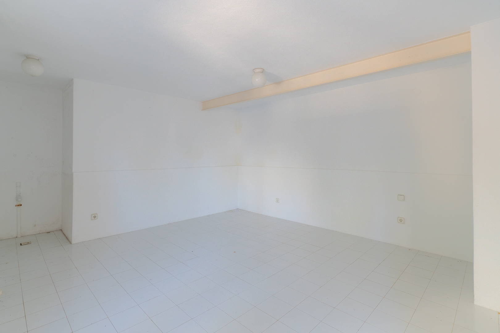 Espace ouvert avec murs blancs, carrelage et éclairage zénithal.