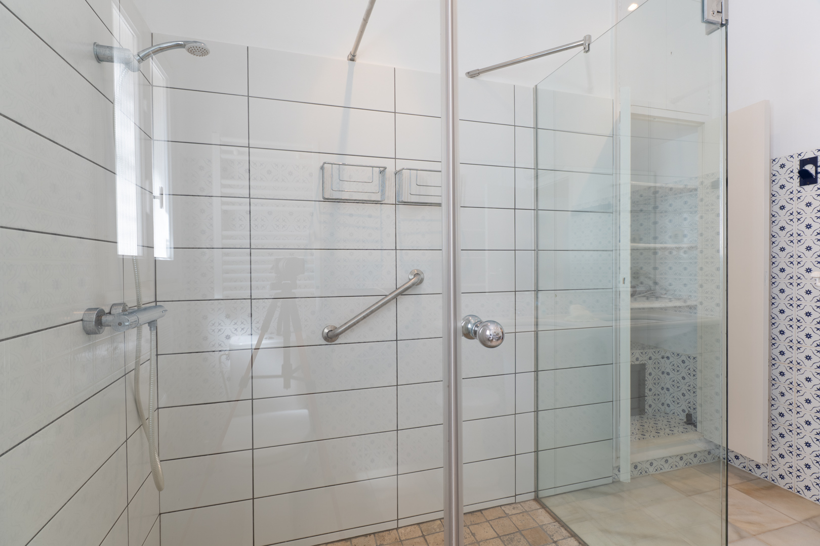 Gros plan de la douche avec paroi en verre et carreaux blancs aux motifs subtils.