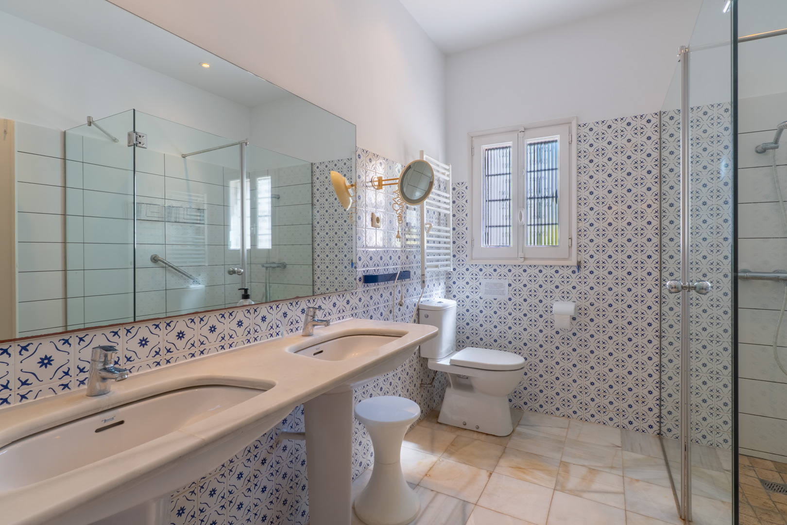 Salle de bain avec double vasque sur colonne, carreaux décoratifs et douche à paroi de verre.