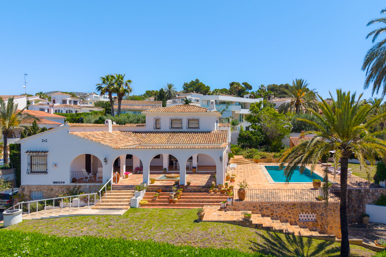 Vue surélevée de la villa avec des arcades, une piscine et un jardin en terrasses avec de la verdure.