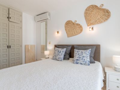Chambre à coucher avec lit confortable, tête de lit grise, couvre-lit blanc matelassé et coussins à motifs. Armoire encastrée à panneaux, climatisation murale et cœurs tressés décoratifs.