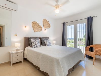 Chambre avec lit double, sol carrelé clair et porte-fenêtre avec rideaux foncés. Profitez de la lumière naturelle, d'un ventilateur de plafond, de la climatisation et d'une vue mer lointaine.