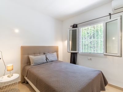 Chambre lumineuse dotée d'un lit avec tête de lit capitonnée, d'une grande fenêtre sécurisée donnant sur la verdure et d'une climatisation intégrée.