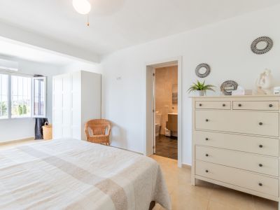 Chambre principale lumineuse avec lit double, armoire blanche et accès direct à une salle de bain attenante. La fenêtre offre une vue sur la végétation.