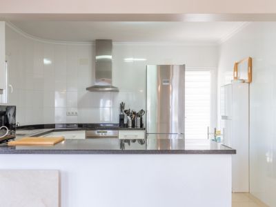 Cuisine moderne et lumineuse avec murs carrelés blancs, plans de travail en granit foncé et appareils électroménagers en acier inoxydable. Un comptoir ouvert offre un espace de travail pratique.