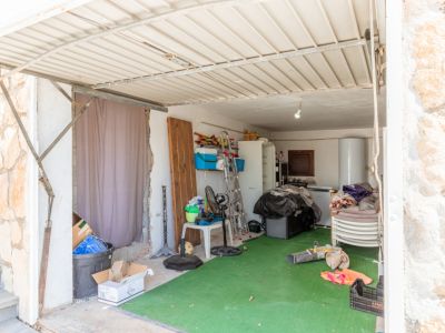 Espace de garage ou de rangement avec un toit en tôle ondulée et un sol en gazon artificiel vert. Il contient un chauffe-eau, un réfrigérateur, une échelle et divers objets stockés.