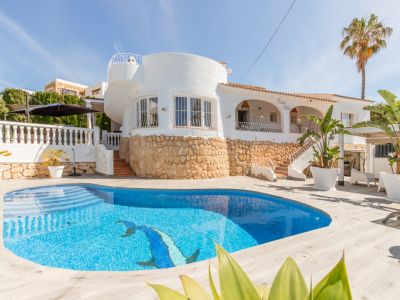 Extérieur d'une villa blanche avec piscine privée carrelée bleue et mosaïque de dauphin. La base en pierre et une section ronde distinctive sont visibles.