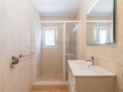 Salle de bain contemporaine avec carrelage mural beige, meuble-lavabo blanc, miroir éclairé par LED et douche à l'italienne avec sol en mosaïque et fenêtre.