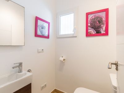 Toilettes d'invités avec lavabo rectangulaire, robinetterie chromée et meuble sous-vasque effet bois foncé. Une fenêtre apporte de la lumière naturelle, agrémentée de cadres roses.