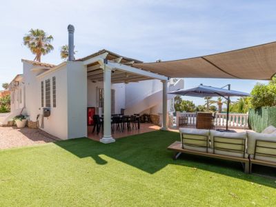 Vaste pelouse artificielle avec canapé extérieur moderne. Terrasse couverte abritant une table à manger et un escalier en colimaçon, sous une voile d'ombrage.