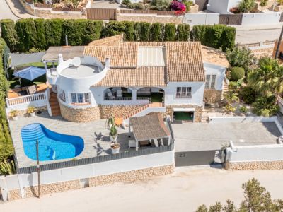 Vue aérienne de la villa blanche avec toit en terre cuite et piscine privée en forme de rein avec mosaïque de dauphin. Elle dispose d'une grande allée pavée et de plusieurs terrasses.