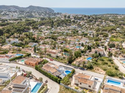 Vue aérienne du quartier résidentiel de Moraira, montrant la densité des villas aux toits de tuiles, des piscines privées et la mer Méditerranée à l'horizon.
